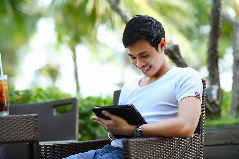 Pria tersenyum saat mengecek catatan keuangan atau mengelola utang menggunakan tablet